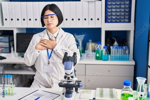 Young asian woman working at scientist laboratory smiling with hands on chest with closed eyes and grateful gesture on face. health concept.