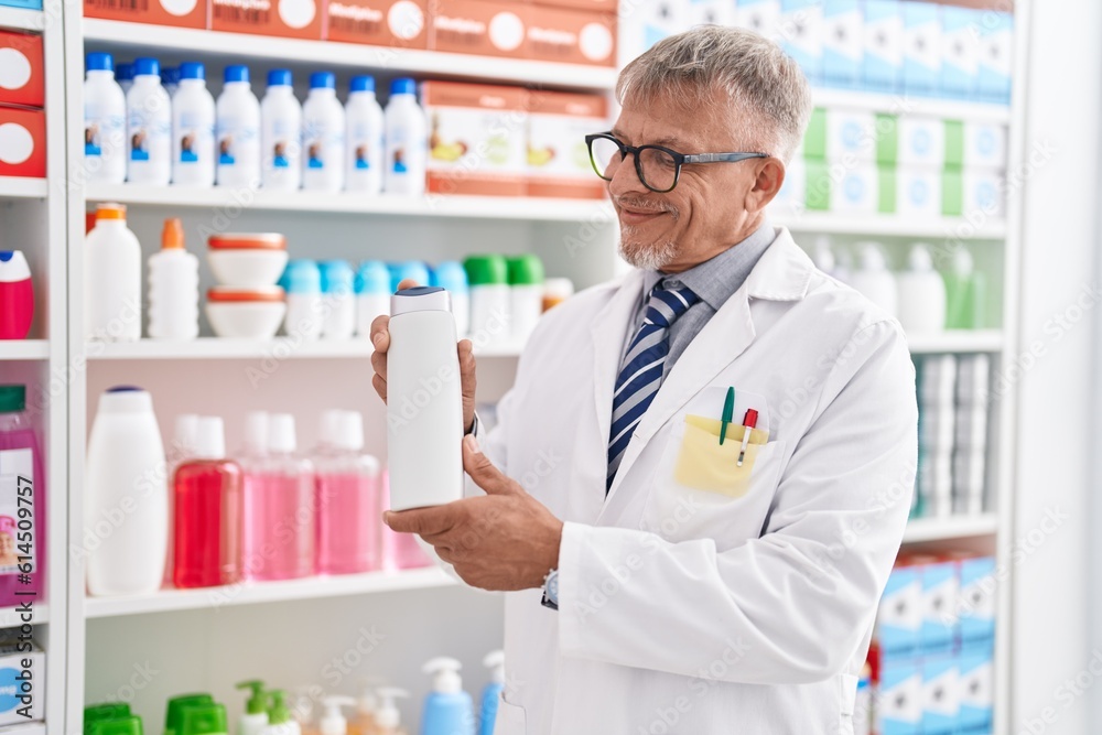 Middle age grey-haired man pharmacist holding shampoo bottle at laboratory Middle age grey-haired man pharmacist holding shampoo bottle at laboratory