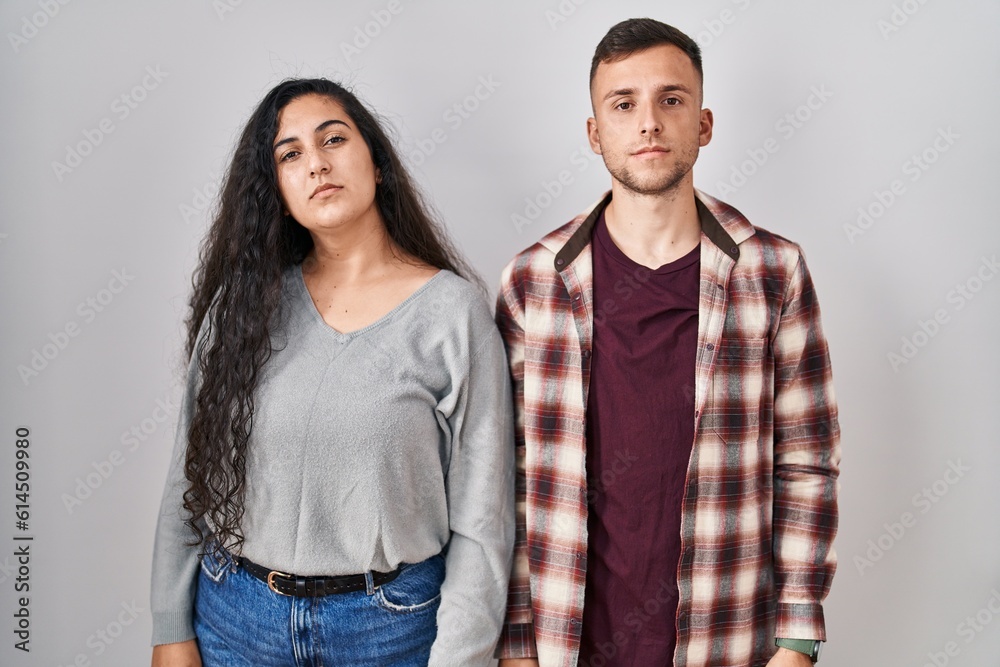 Young hispanic couple standing over white background relaxed with serious expression on face. simple and natural looking at the camera. Young hispanic couple standing over white background relaxed with serious expression on face. simple and natural looking at the camera.