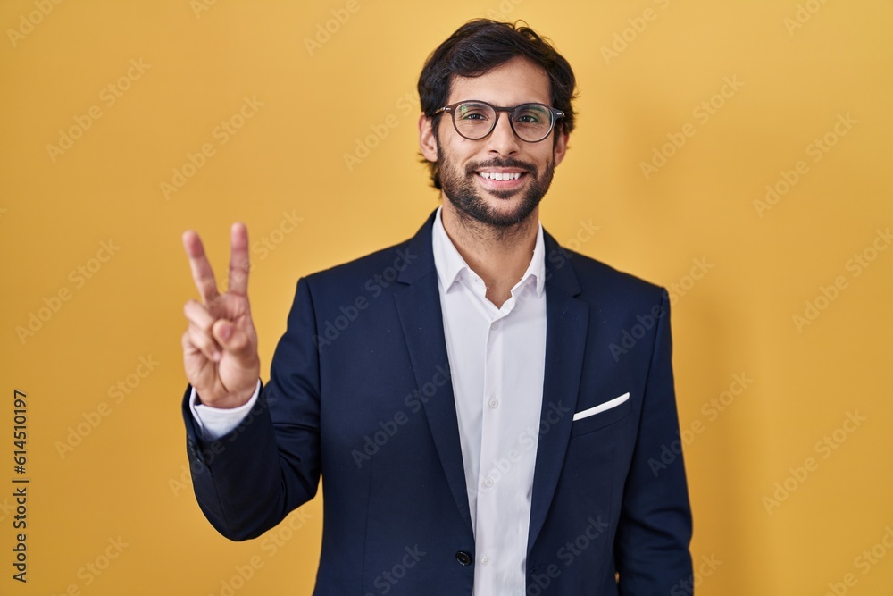 Handsome latin man standing over yellow background showing and pointing up with fingers number two while smiling confident and happy. Handsome latin man standing over yellow background showing and pointing up with fingers number two while smiling confident and happy.