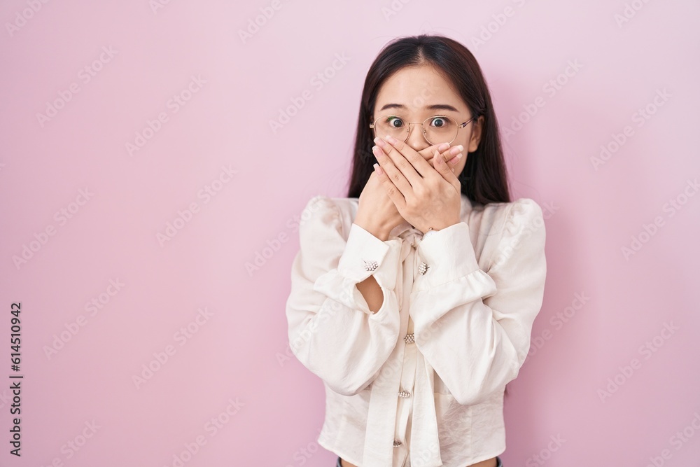 Young chinese woman standing over pink background shocked covering mouth with hands for mistake. secret concept. Young chinese woman standing over pink background shocked covering mouth with hands for mistake. secret concept.