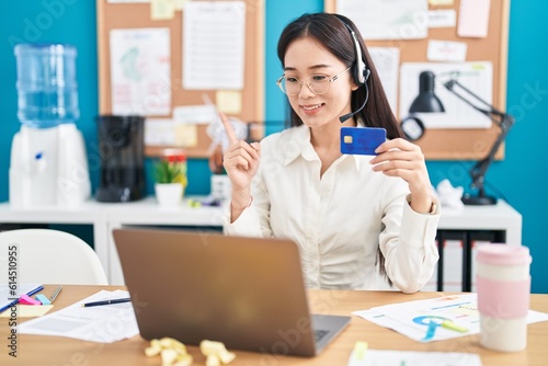 Young chinese woman working at the office doing online shopping smiling happy pointing with hand and finger to the side
