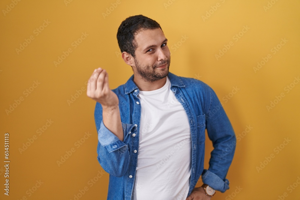Hispanic man standing over yellow background doing italian gesture with hand and fingers confident expression