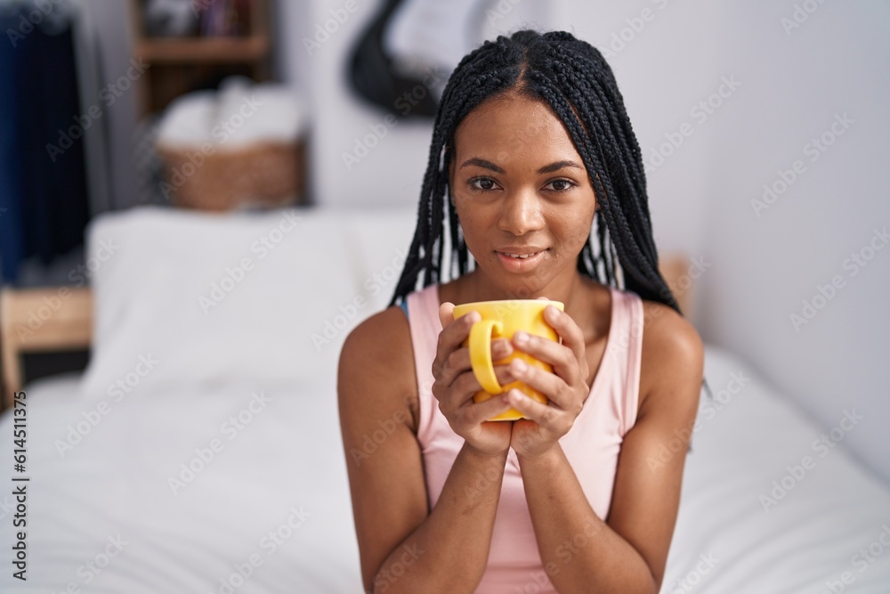 African american woman drinking cup of coffee sitting on bed at bedroom