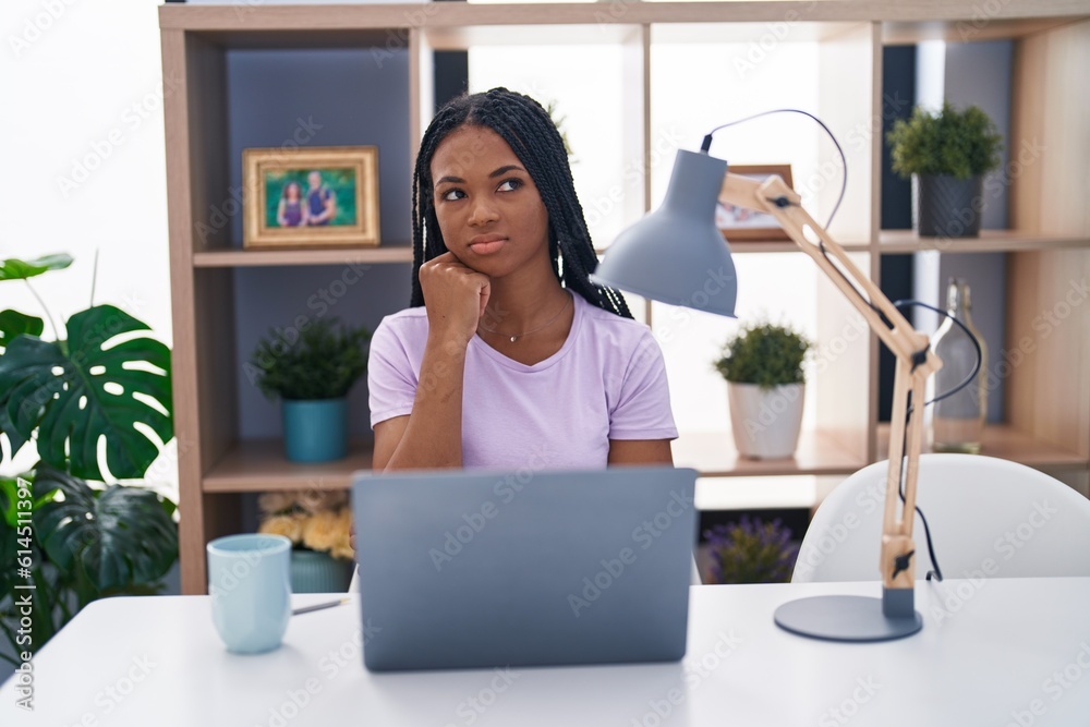 African american woman with braids using laptop at home serious face thinking about question with hand on chin, thoughtful about confusing idea African american woman with braids using laptop at home serious face thinking about question with hand on chin, thoughtful about confusing idea