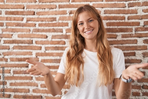 Young caucasian woman standing over bricks wall smiling cheerful offering hands giving assistance and acceptance.
