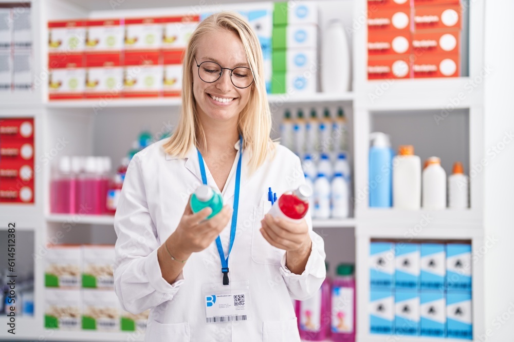 Young blonde woman pharmacist smiling confident holding medication bottles at pharmacy