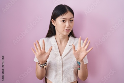 Quadro su tela Chinese young woman standing over pink background moving away hands palms showing refusal and denial with afraid and disgusting expression