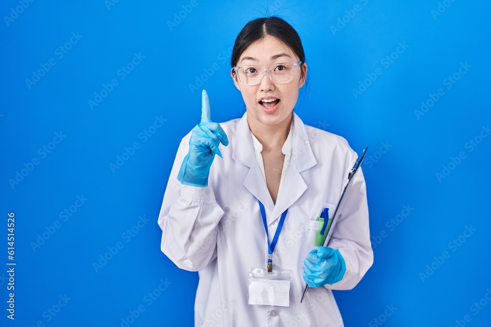 Chinese young woman working at scientist laboratory smiling amazed and surprised and pointing up with fingers and raised arms. Chinese young woman working at scientist laboratory smiling amazed and surprised and pointing up with fingers and raised arms.