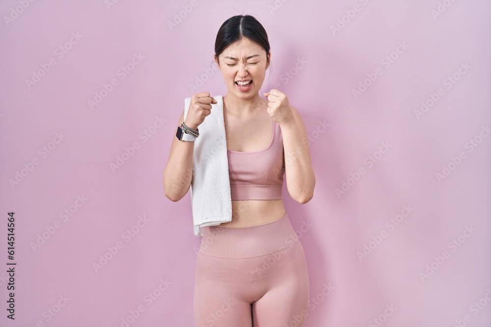 Chinese young woman wearing sportswear and towel excited for success with arms raised and eyes closed celebrating victory smiling. winner concept. Chinese young woman wearing sportswear and towel excited for success with arms raised and eyes closed celebrating victory smiling. winner concept.