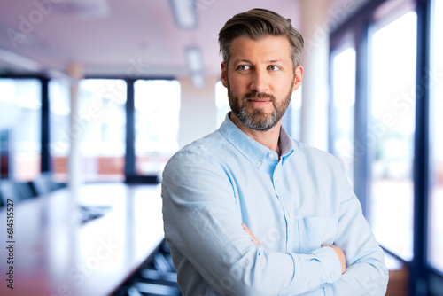 Confident businessman standing with arms crossed at the office