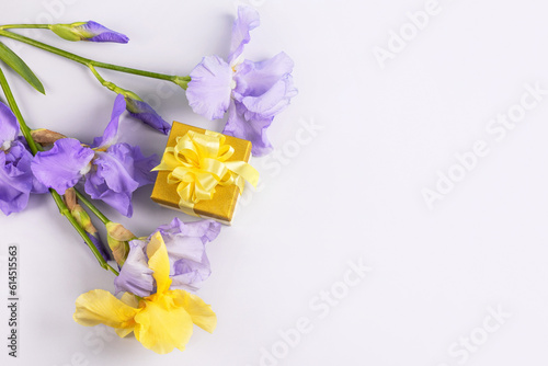 Greeting card for mother's day, Valentine's Day, birthday. Yellow gift box with a satin ribbon bow and purple iris flowers on a blue background with a place for your text. © Katya Slavashevich