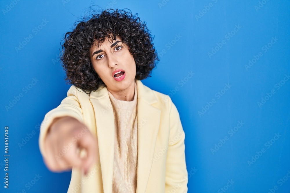 Young brunette woman with curly hair standing over blue background pointing displeased and frustrated to the camera, angry and furious with you Young brunette woman with curly hair standing over blue background pointing displeased and frustrated to the camera, angry and furious with you