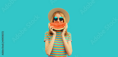 Summer portrait of happy smiling young woman with fresh juicy slice of watermelon wearing straw hat on blue background