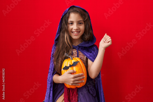 Little hispanic girl wearing witch halloween costume screaming proud, celebrating victory and success very excited with raised arms photo