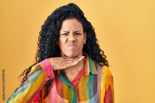 Middle age hispanic woman standing over yellow background cutting throat with hand as knife, threaten aggression with furious violence © Krakenimages.com