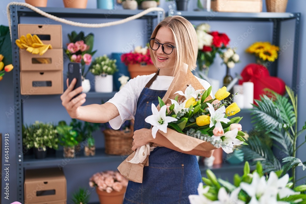 Young blonde woman florist make selfie by smartphone holding bouquet of flowers at florist shop