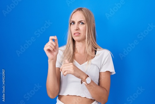 Young caucasian woman standing over blue background disgusted expression, displeased and fearful doing disgust face because aversion reaction. © Krakenimages.com