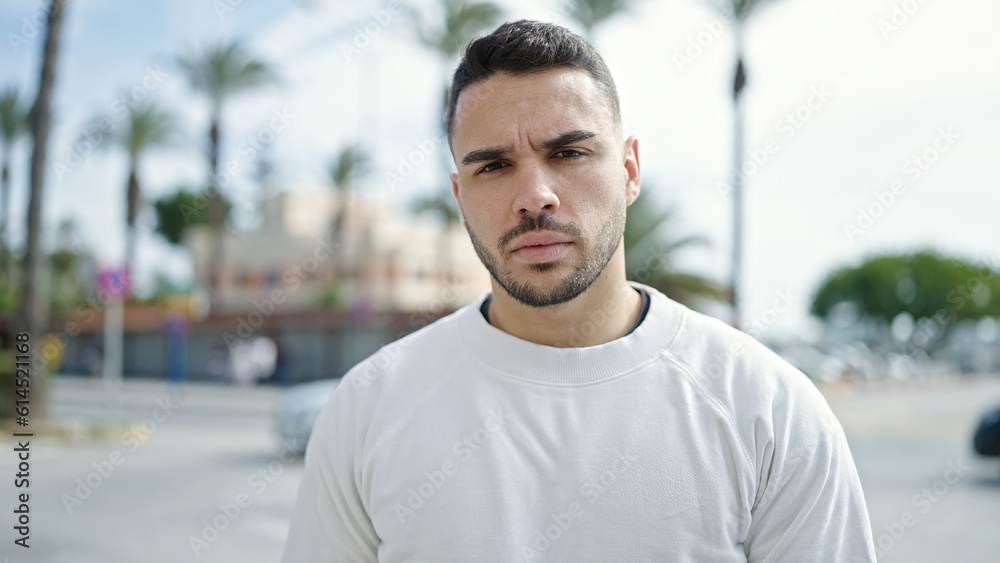 Young hispanic man standing with serious expression at street