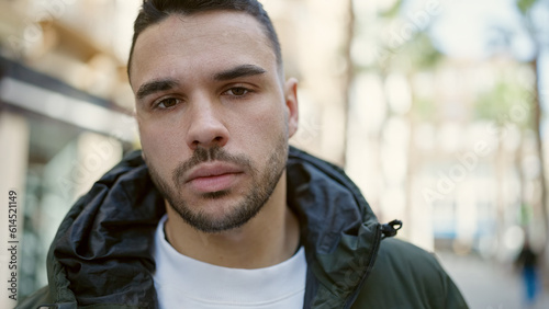 Young hispanic man standing with serious expression at street