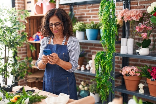 Middle age woman florist smiling confident using smartphone at flower shop
