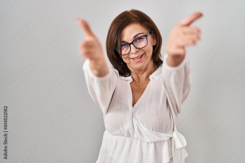 Middle age hispanic woman standing over isolated background looking at the camera smiling with open arms for hug. cheerful expression embracing happiness. Middle age hispanic woman standing over isolated background looking at the camera smiling with open arms for hug. cheerful expression embracing happiness.