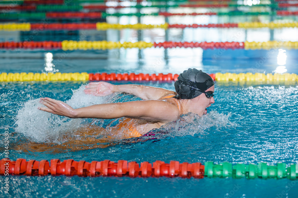 Female competitive swimmer moving through the water performing the butterfly stroke during swimming training, front view.