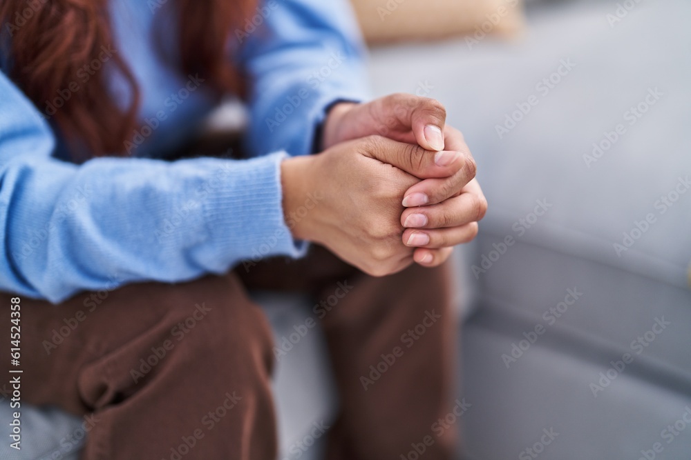 Fototapeta premium Young hispanic woman sitting on sofa with hands together at home