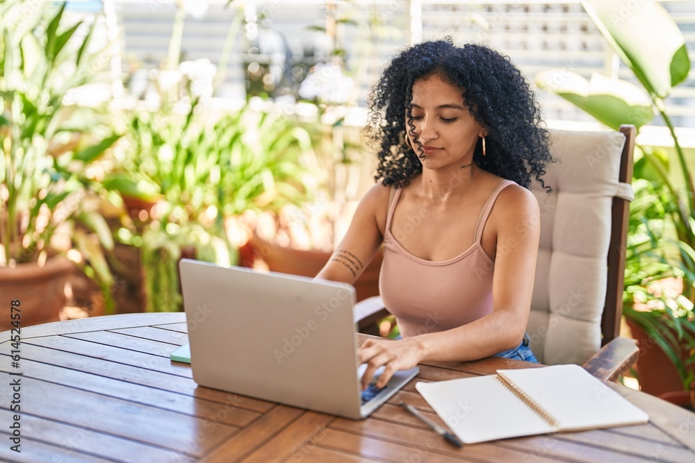 Young hispanic woman using laptop sitting on table at home terrace