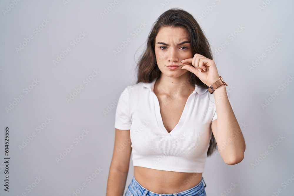 Fototapeta premium Young teenager girl standing over white background mouth and lips shut as zip with fingers. secret and silent, taboo talking