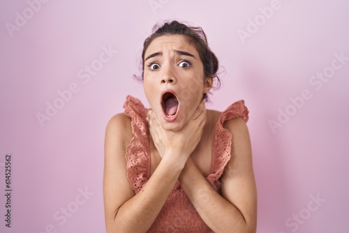 Young teenager girl standing over pink background shouting and suffocate because painful strangle. health problem. asphyxiate and suicide concept.