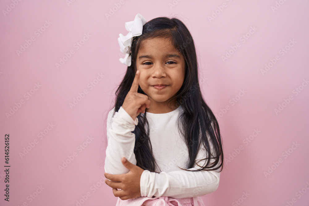 Little hispanic girl standing over pink background smiling with an idea or question pointing finger with happy face, number one Little hispanic girl standing over pink background smiling with an idea or question pointing finger with happy face, number one