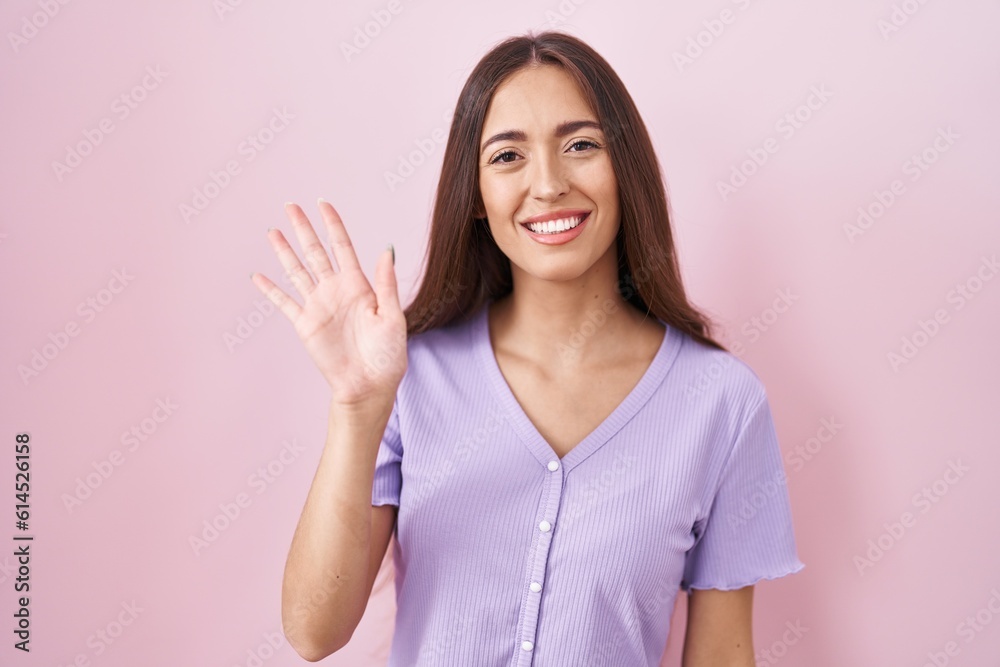 Young hispanic woman with long hair standing over pink background waiving saying hello happy and smiling, friendly welcome gesture Young hispanic woman with long hair standing over pink background waiving saying hello happy and smiling, friendly welcome gesture