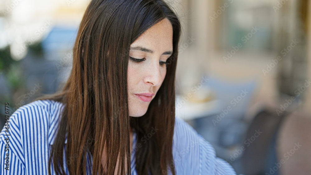 Young beautiful hispanic woman looking to the side with serious expression sitting on table at coffee shop terrace Young beautiful hispanic woman looking to the side with serious expression sitting on table at coffee shop terrace