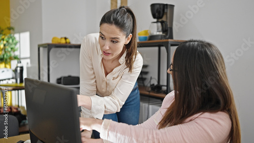 Two women business workers using computer speaking at office