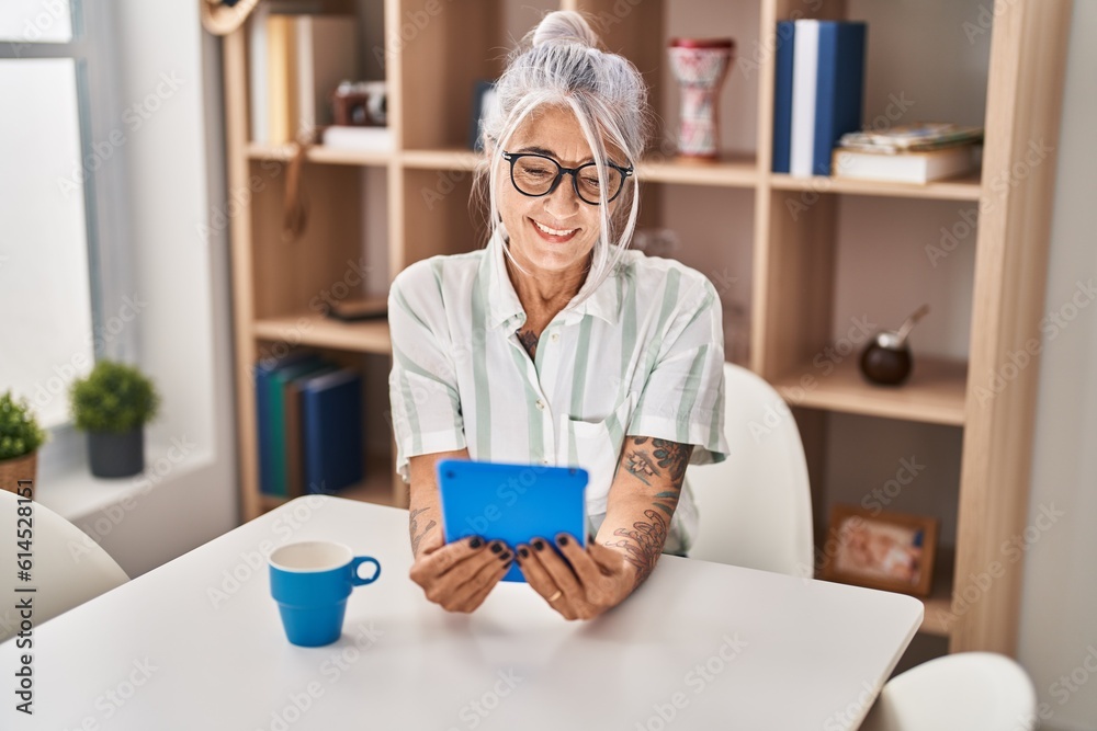 Middle age grey-haired woman drinking coffee and using touchpad at home Middle age grey-haired woman drinking coffee and using touchpad at home