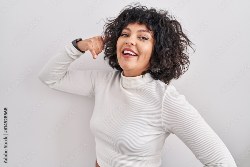 Hispanic woman with curly hair standing over isolated background smiling doing phone gesture with hand and fingers like talking on the telephone. communicating concepts. Hispanic woman with curly hair standing over isolated background smiling doing phone gesture with hand and fingers like talking on the telephone. communicating concepts.
