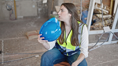 Young beautiful hispanic woman builder tired using hardhat as a hand fan at construction site photo