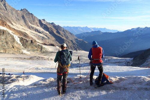 Mountaineers with crampons preparing the rope for ascent to mountain Allalinhorn and snow mountain panorama in Pennine Alps, Switzerland