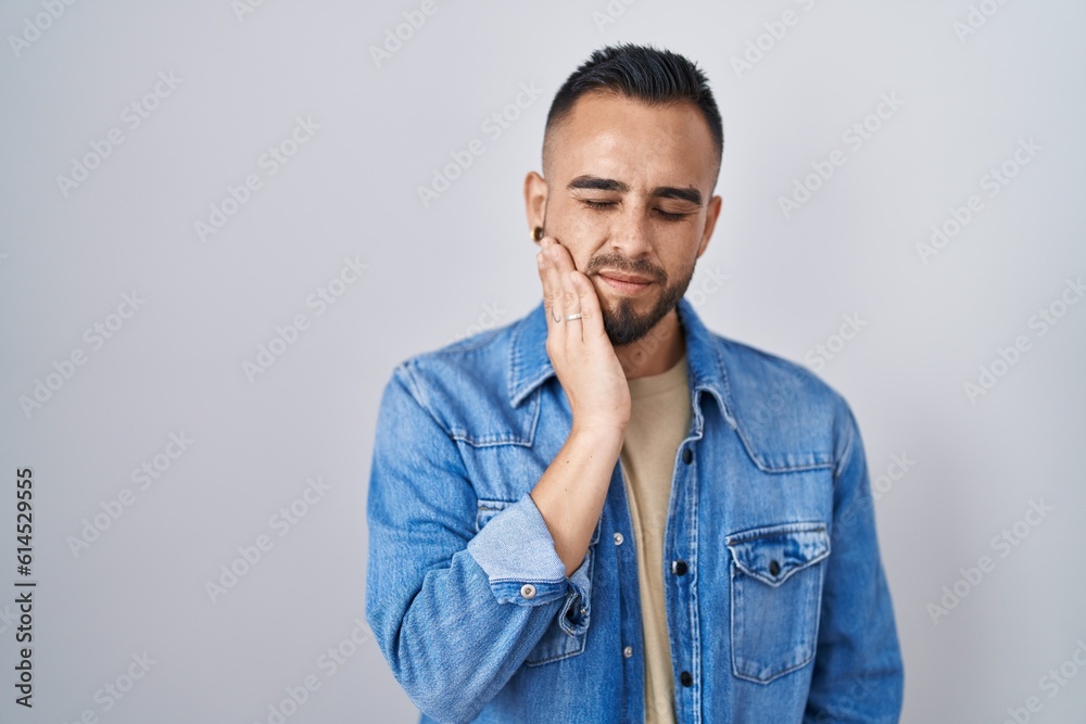 Young hispanic man standing over isolated background touching mouth with hand with painful expression because of toothache or dental illness on teeth. dentist Young hispanic man standing over isolated background touching mouth with hand with painful expression because of toothache or dental illness on teeth. dentist