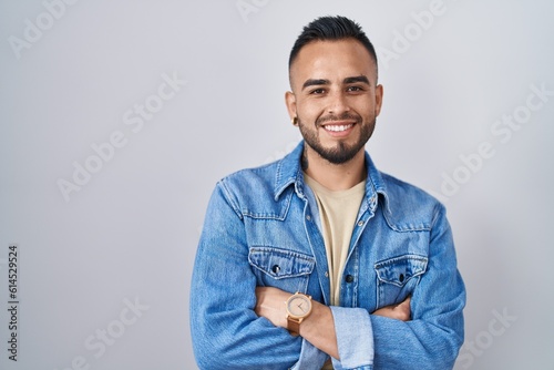 Young hispanic man standing over isolated background happy face smiling with crossed arms looking at the camera. positive person.