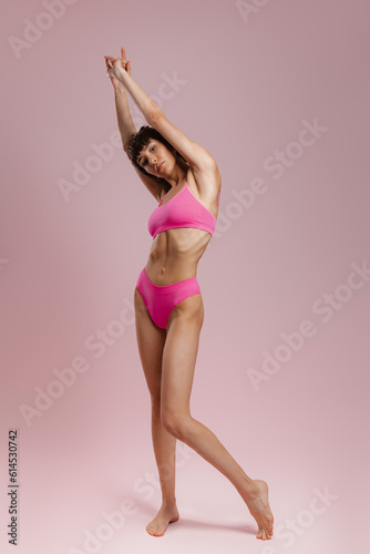 Full length of young short hair woman in underwear stretching against colored background © gstockstudio