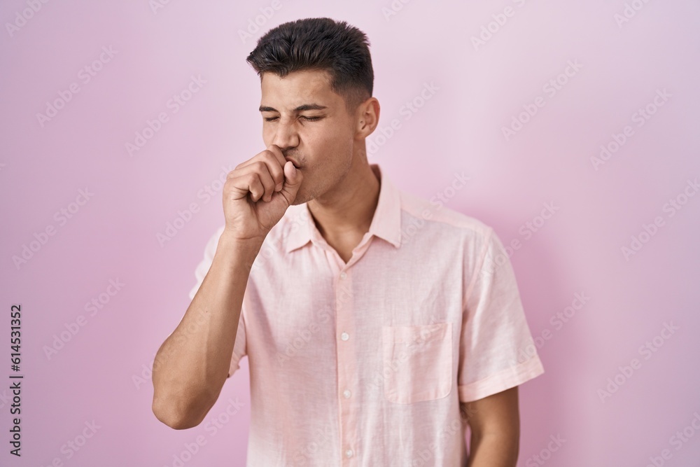 Young hispanic man standing over pink background feeling unwell and coughing as symptom for cold or bronchitis. health care concept. Young hispanic man standing over pink background feeling unwell and coughing as symptom for cold or bronchitis. health care concept.