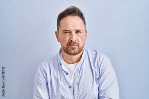Middle age caucasian man standing over blue background with hand on stomach because indigestion, painful illness feeling unwell. ache concept.