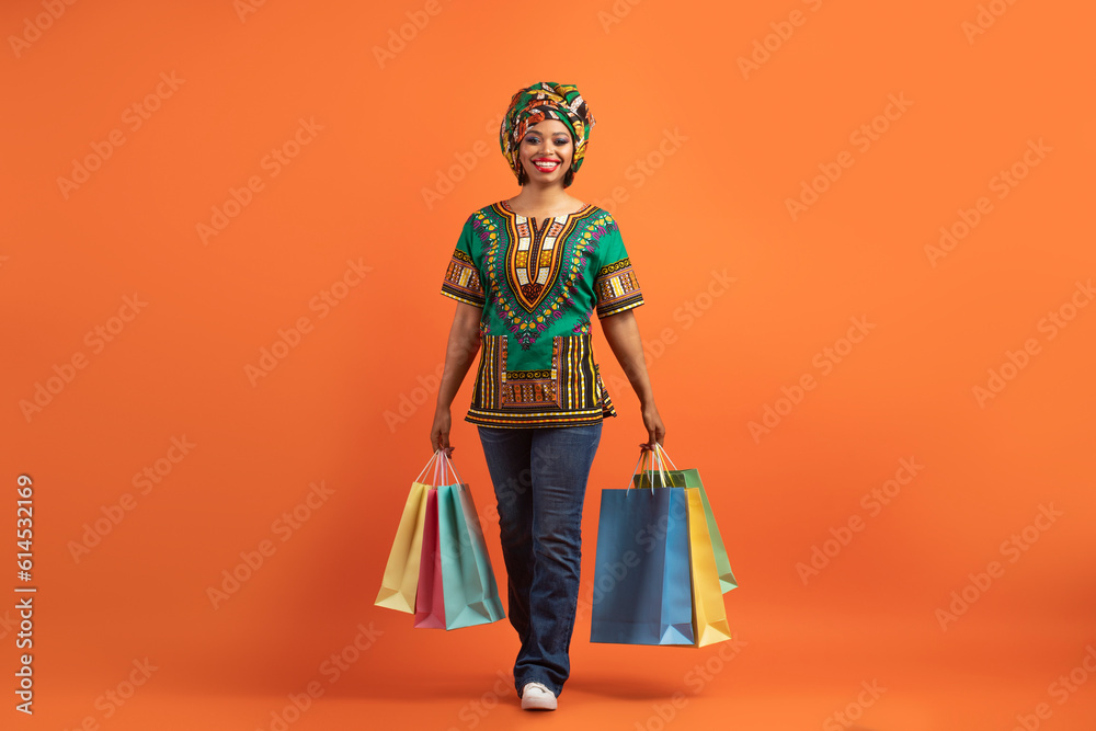 Happy black lady in african costume walking with her purchases