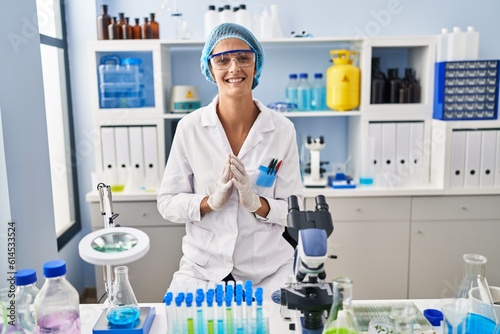 Brunette woman working at scientist laboratory hands together and fingers crossed smiling relaxed and cheerful. success and optimistic