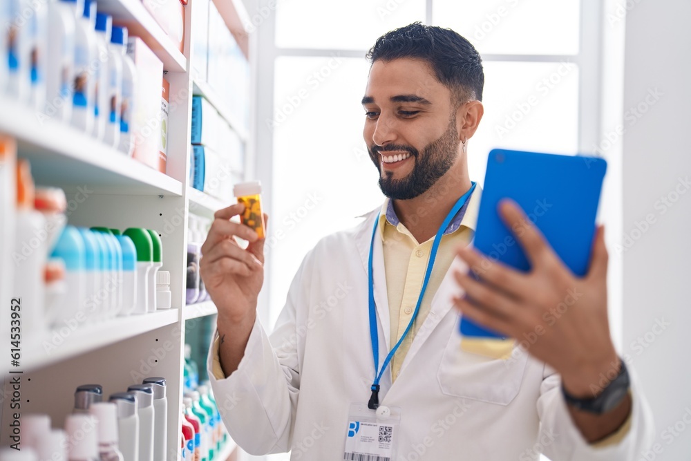 Young arab man pharmacist using touchpad holding pills bottle at pharmacy