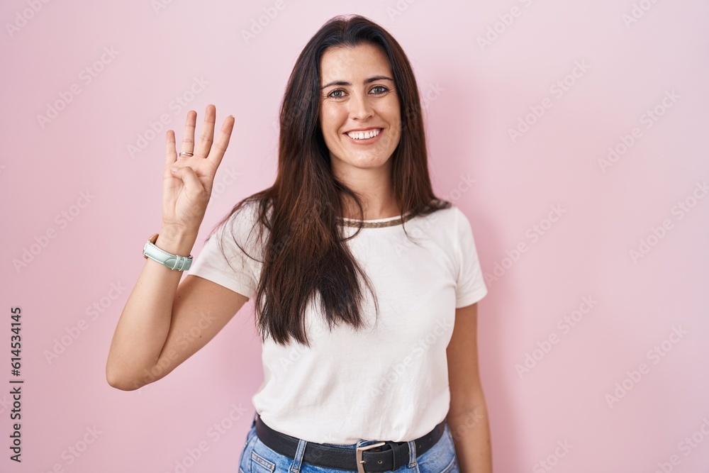 Young brunette woman standing over pink background showing and pointing up with fingers number four while smiling confident and happy. Young brunette woman standing over pink background showing and pointing up with fingers number four while smiling confident and happy.