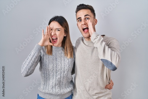 Young hispanic couple standing over white background shouting and screaming loud to side with hand on mouth. communication concept.