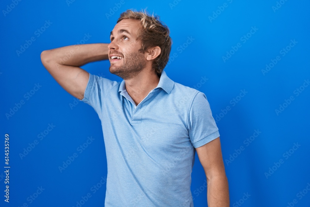 Caucasian man standing over blue background smiling confident touching hair with hand up gesture, posing attractive and fashionable Caucasian man standing over blue background smiling confident touching hair with hand up gesture, posing attractive and fashionable